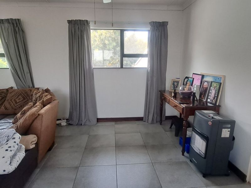 A living room area featuring neutral tiled flooring, aluminium window frames, and a ceiling fan, offering a functional and well-lit space.