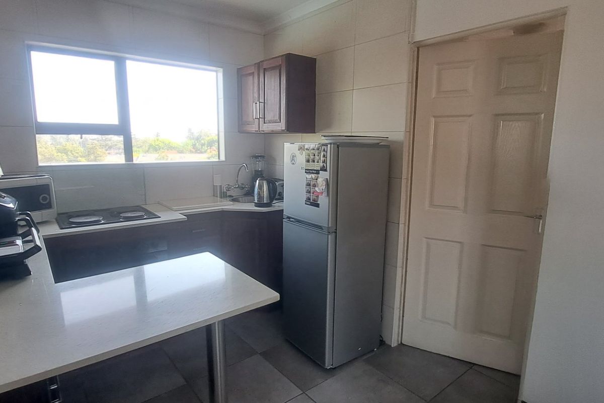 A functional kitchen featuring built-in cabinetry, stone countertops, an electric hob, and tiled finishes, offering a practical layout for daily meal preparation.
