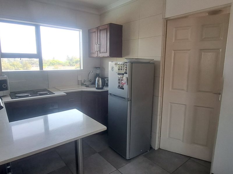 A functional kitchen featuring built-in cabinetry, stone countertops, an electric hob, and tiled finishes, offering a practical layout for daily meal preparation.