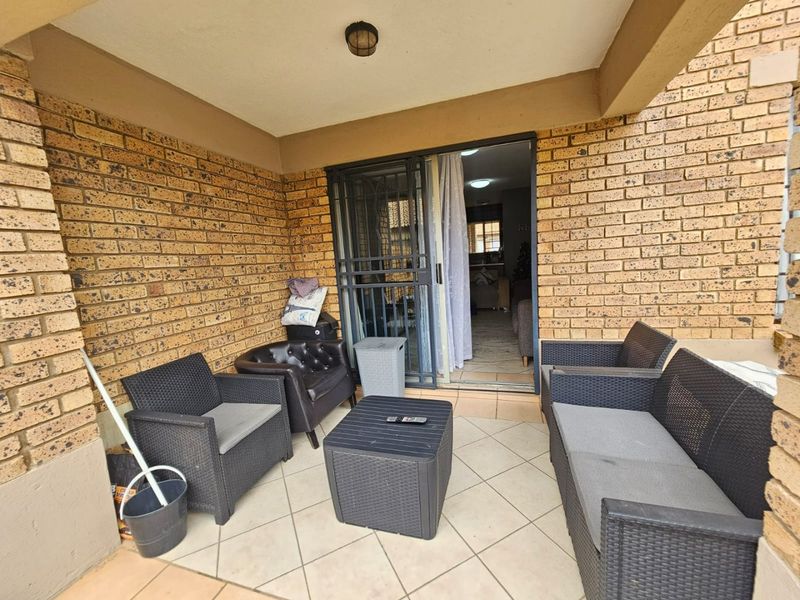 Covered patio area featuring exposed brick walls, tiled flooring, and a secure sliding door entrance leading into the apartment.