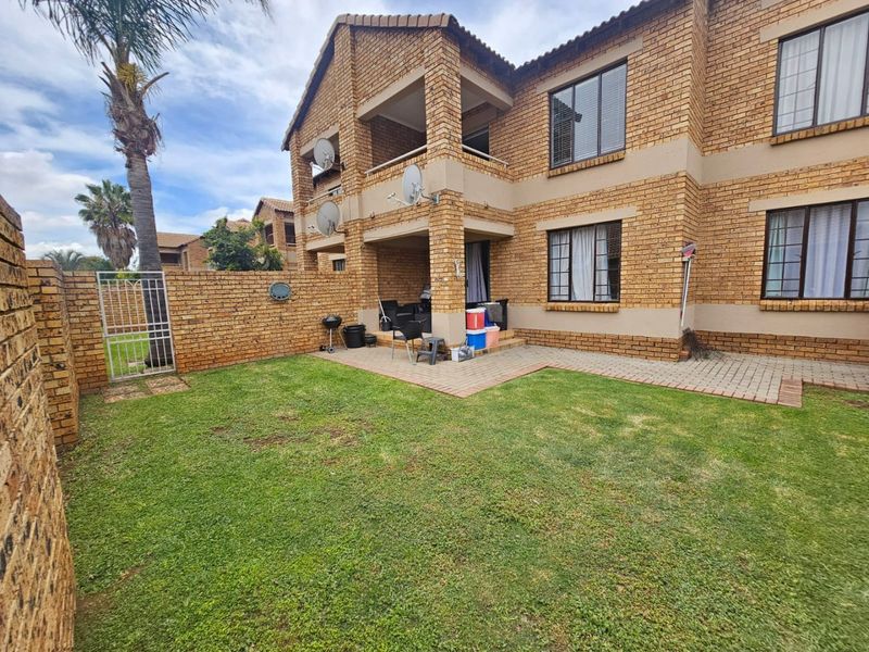 Rear view of a face brick apartment building featuring a private garden, paved patio area, and secure boundary wall.