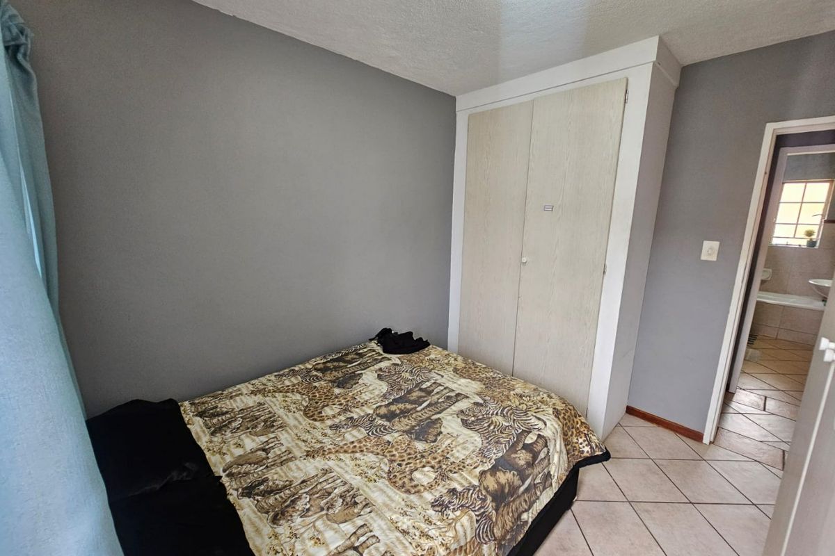 A bedroom featuring tiled flooring, a built-in wardrobe, and neutral grey walls, with direct access to an adjacent bathroom.