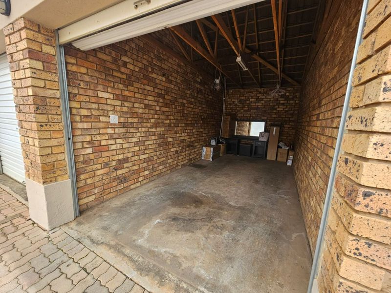 A functional single-car garage featuring exposed brick walls, concrete flooring, and exposed timber roof trusses, providing secure storage or parking space.