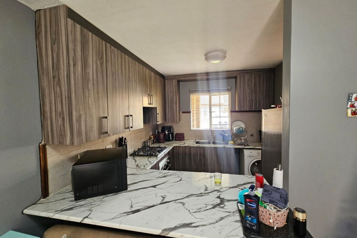 A functional kitchen featuring wood-grain cabinetry, marble-effect countertops, a gas hob, built-in oven, and a convenient breakfast bar area.