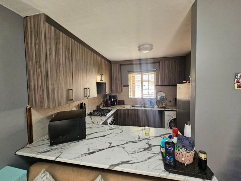 A functional kitchen featuring wood-grain cabinetry, marble-effect countertops, a gas hob, built-in oven, and a convenient breakfast bar area.