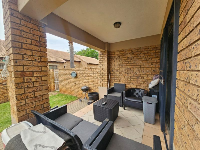 A covered patio area featuring exposed brick walls, tiled flooring, and a security gate, providing a functional outdoor space for relaxation.