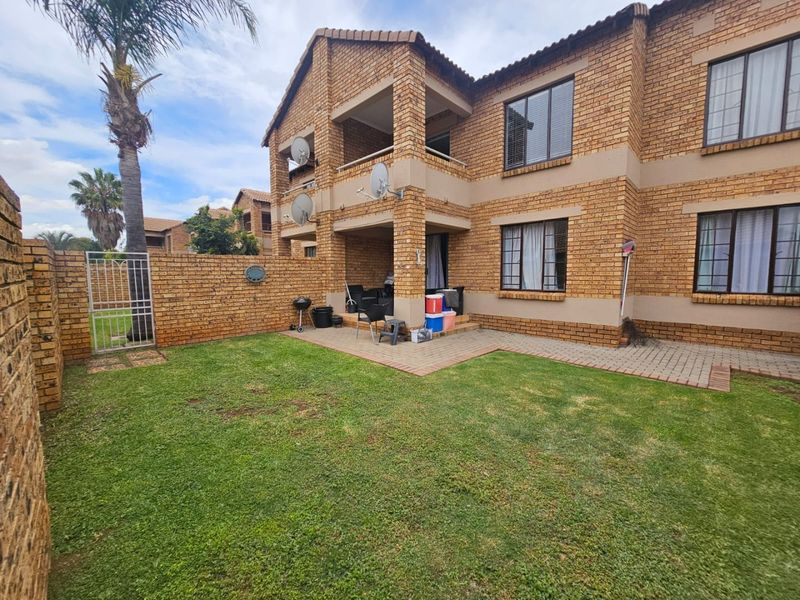 Rear view of a face brick apartment building featuring a private garden, paved patio area, and secure perimeter walling.