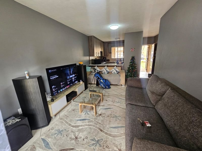 Open plan living area featuring tiled flooring and a compact kitchen with built-in cabinetry, leading directly to the apartment entrance.