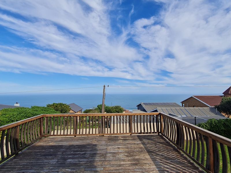 An elevated wooden deck balcony offering expansive ocean views, featuring a timber balustrade and weathered decking.