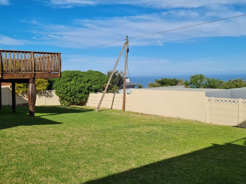 A spacious backyard featuring a well-maintained lawn, a raised wooden deck, and a precast concrete boundary wall with distant ocean views.