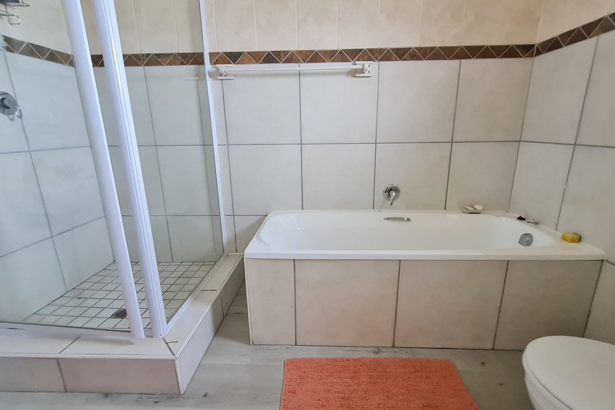 A functional bathroom featuring a separate shower enclosure, a built-in bathtub, and neutral wall tiling.