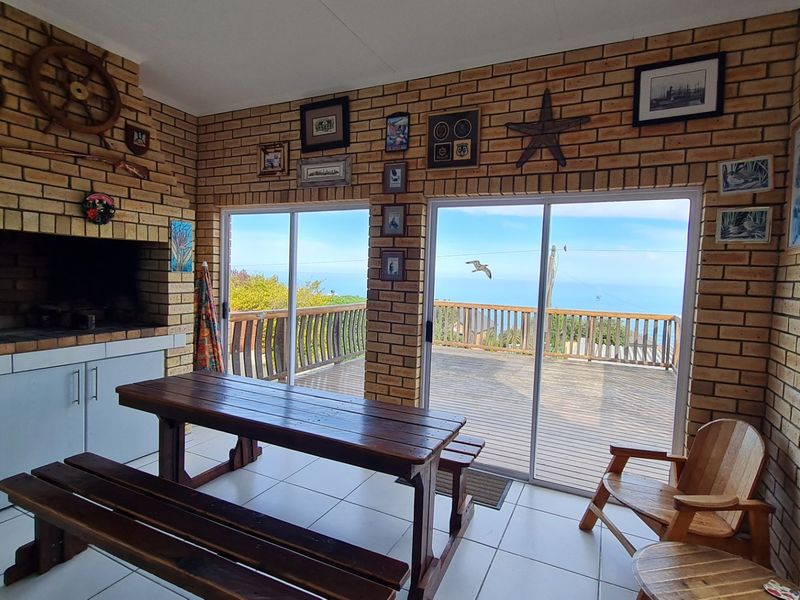 Covered patio area featuring a built-in braai, exposed brick walls, and sliding glass doors opening onto a wooden deck with scenic ocean views.