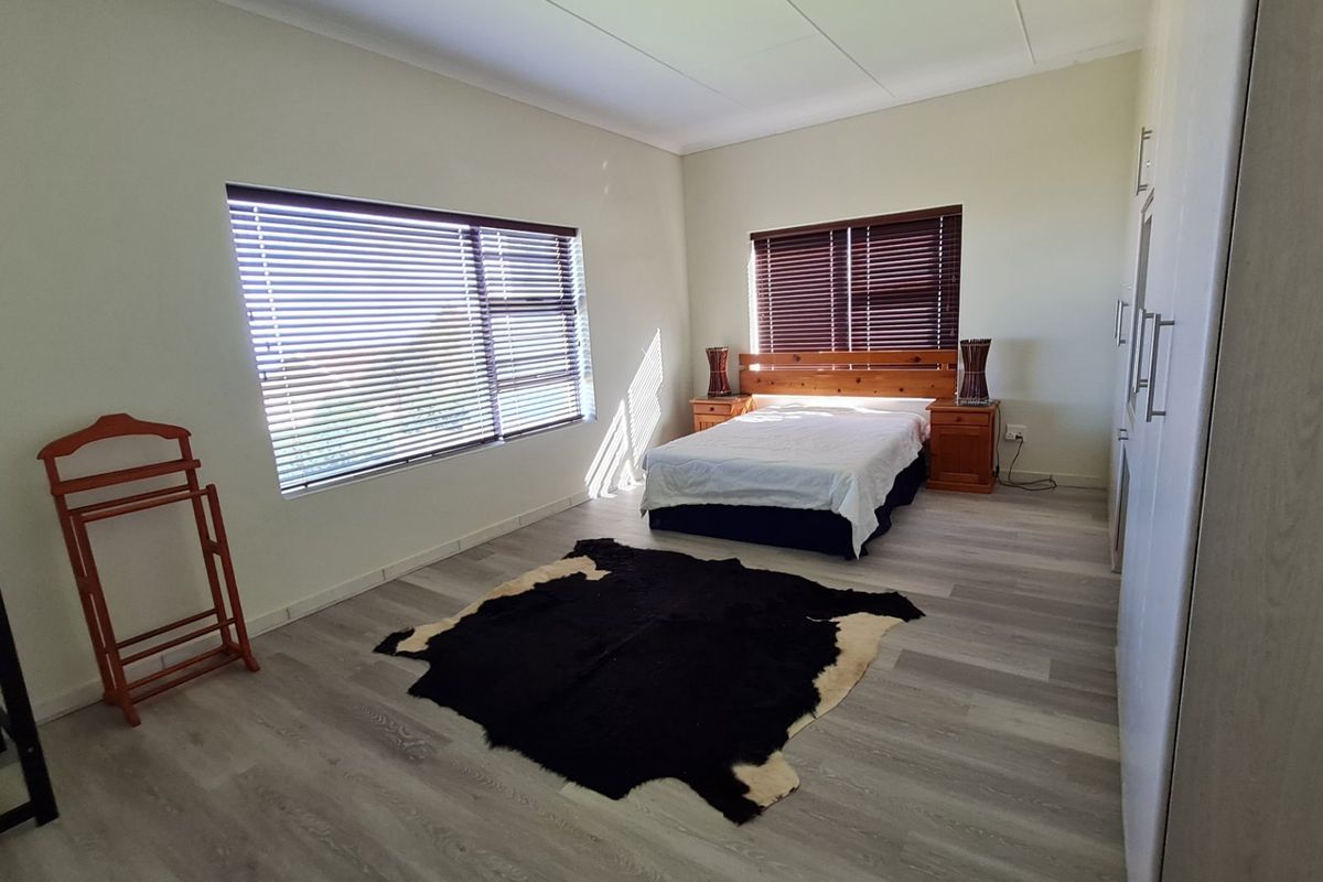 Spacious bedroom featuring modern laminate flooring, built-in cupboards, and large windows with venetian blinds for natural light control.