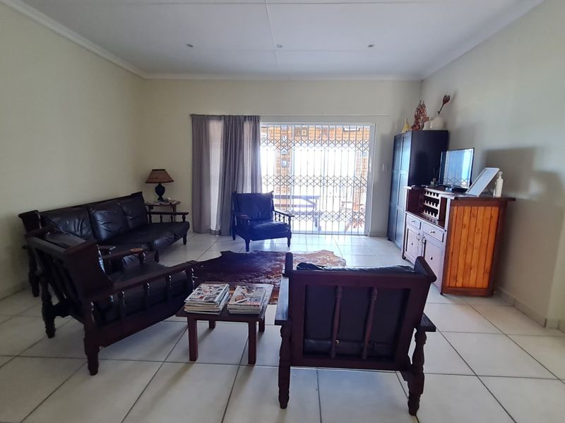 Spacious living room featuring neutral tiled flooring and a sliding glass door with security gate providing access to the outdoor area.