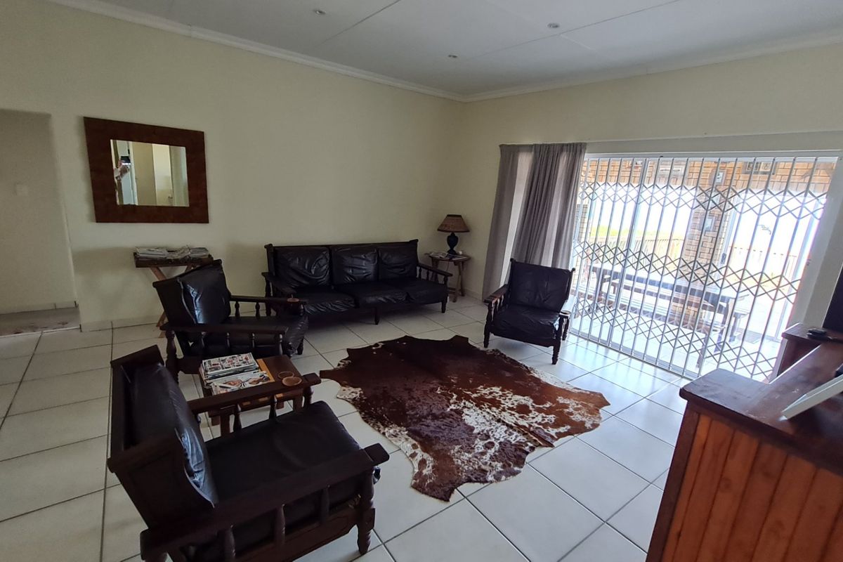 A spacious living room featuring neutral tiled flooring and a large sliding glass door with a security gate, providing access to the outdoor area.
