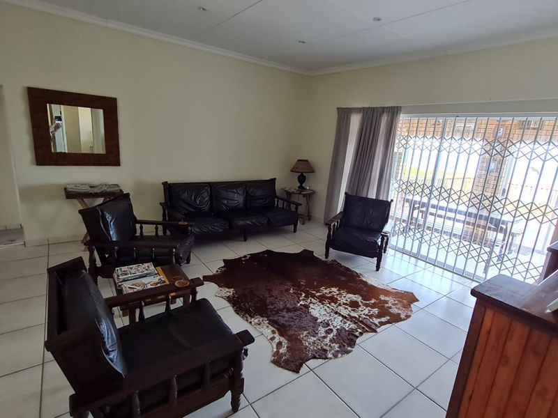 A spacious living room featuring neutral tiled flooring and a large sliding glass door with a security gate, providing access to the outdoor area.