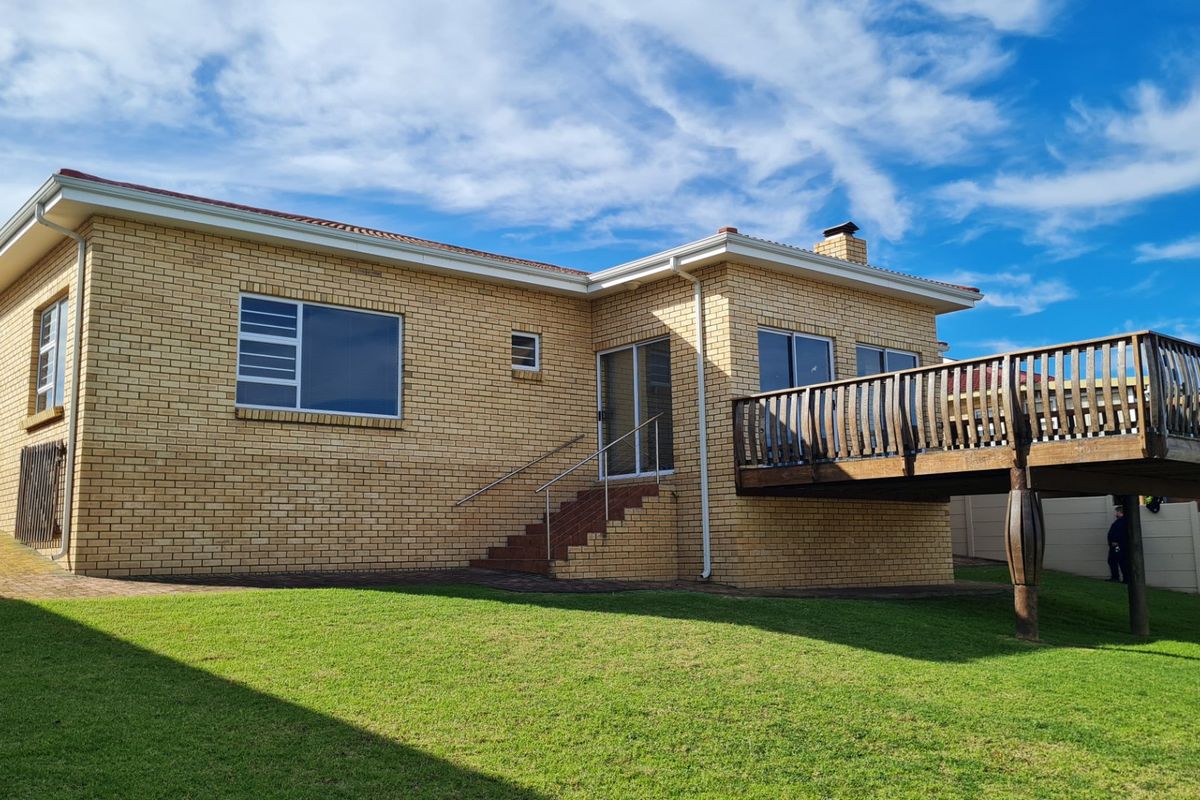 Rear view of a brick house featuring a raised wooden deck, sliding glass doors, and a well-maintained lawn.
