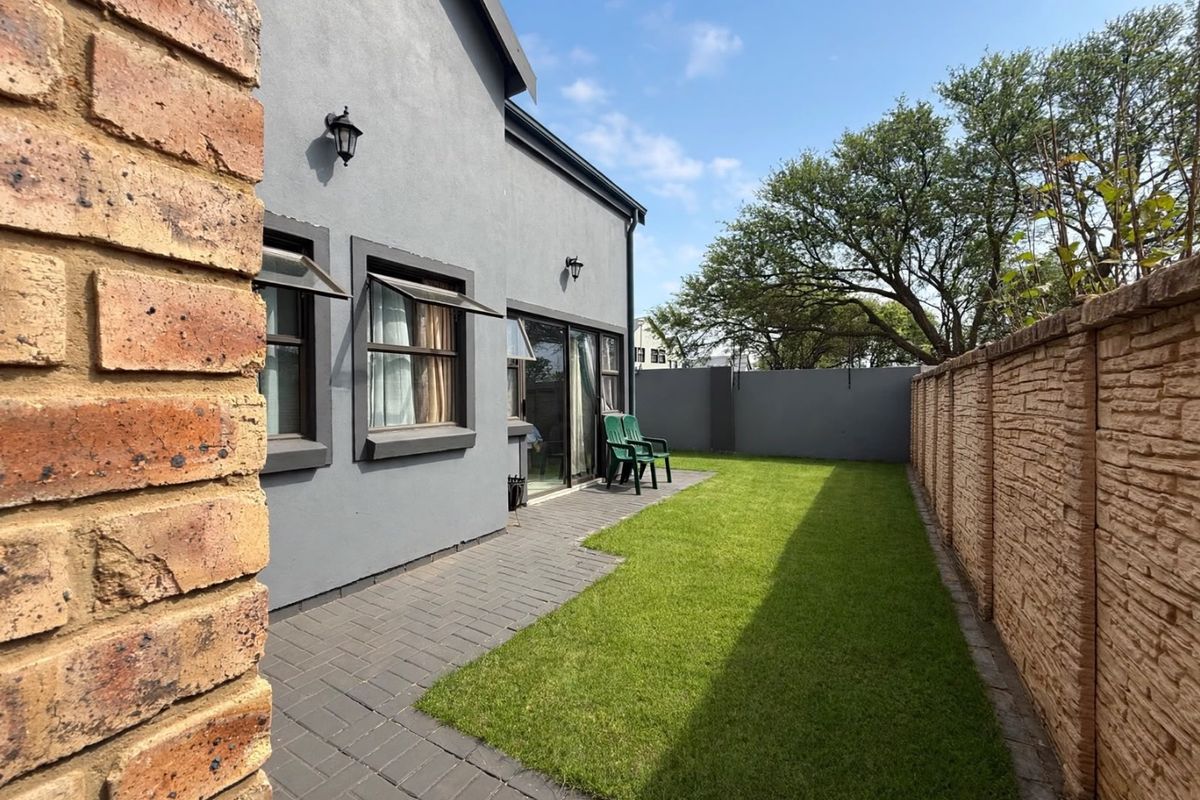A well-maintained rear garden featuring a paved patio area, a neat lawn, and a secure brick boundary wall.