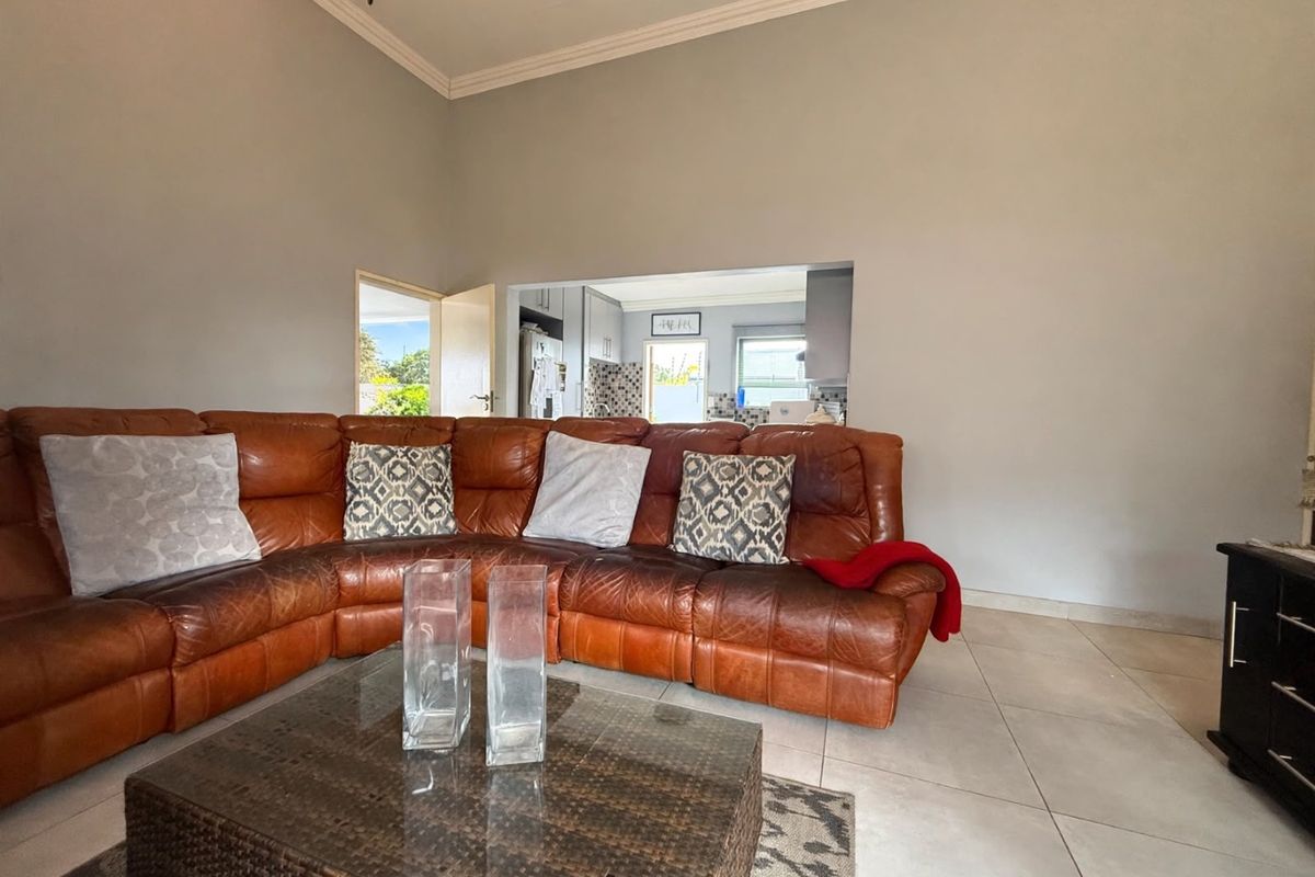 Spacious living room featuring tiled flooring and coved ceilings, with an open-plan flow leading through to the kitchen area.