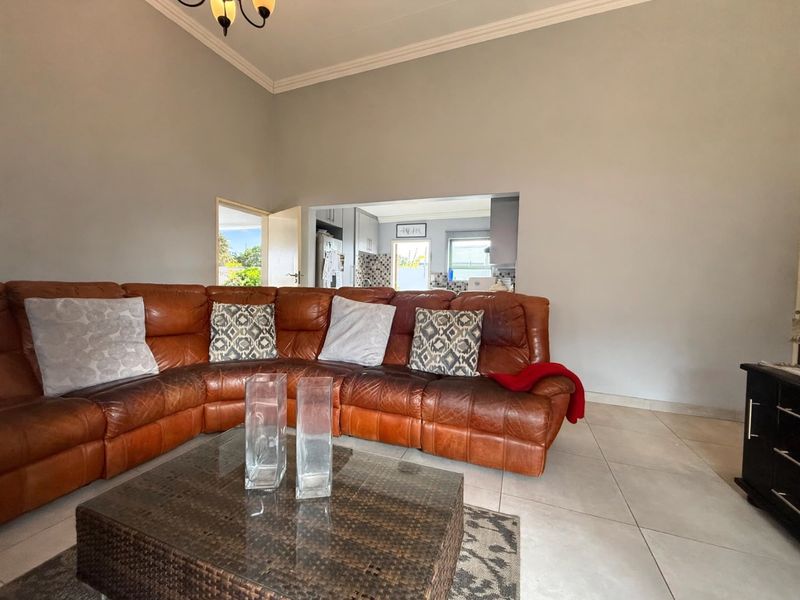Spacious living room featuring tiled flooring and coved ceilings, with an open-plan flow leading through to the kitchen area.