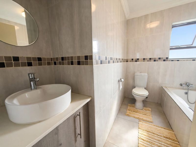 A well-maintained bathroom featuring a modern vessel sink on a vanity cabinet, a toilet, and a bathtub with tiled finishes throughout.