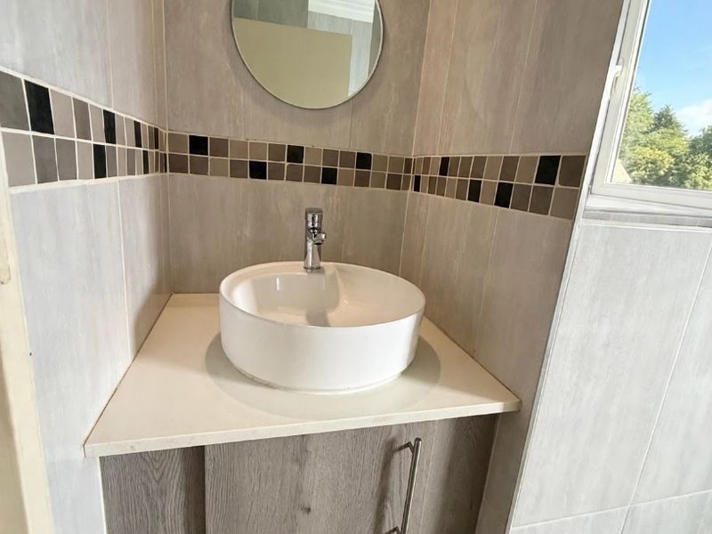 A modern bathroom vanity area featuring a white vessel sink, wood-grain cabinetry, and decorative mosaic tile accents.