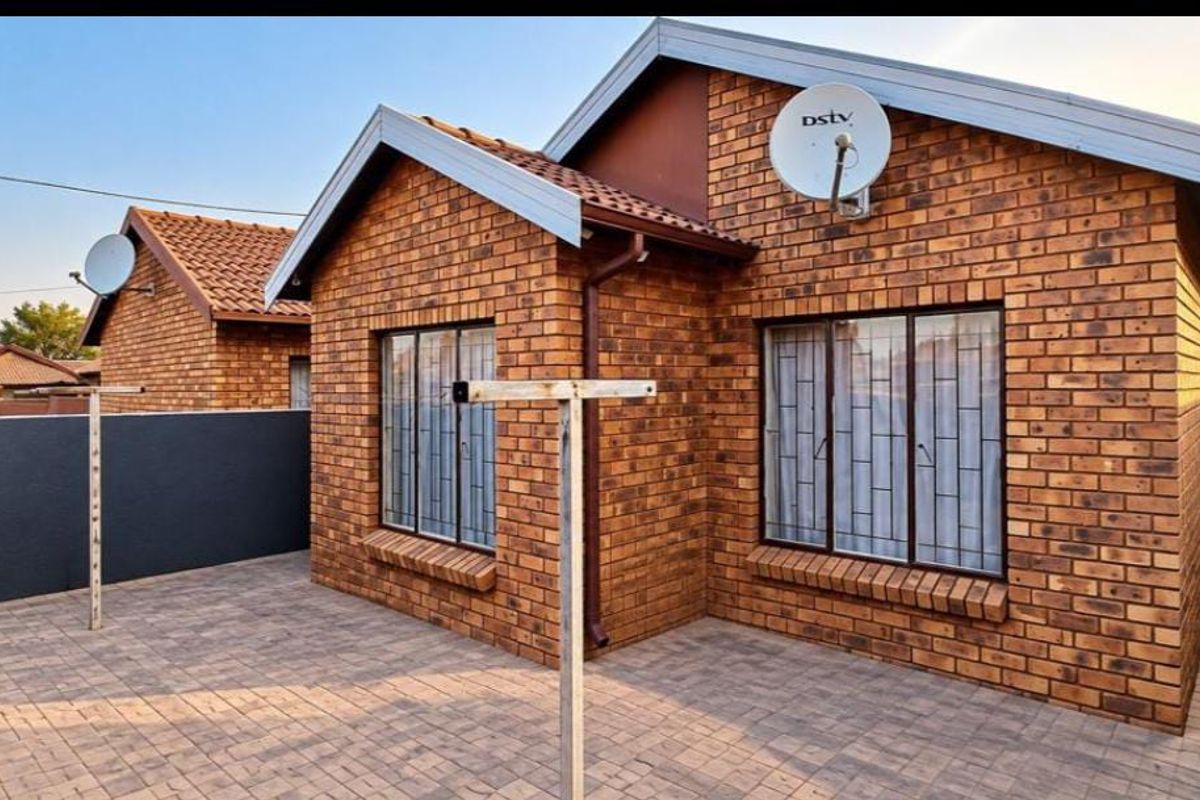 A well-maintained face brick exterior featuring a paved patio area, secure window bars, and tiled roofing.