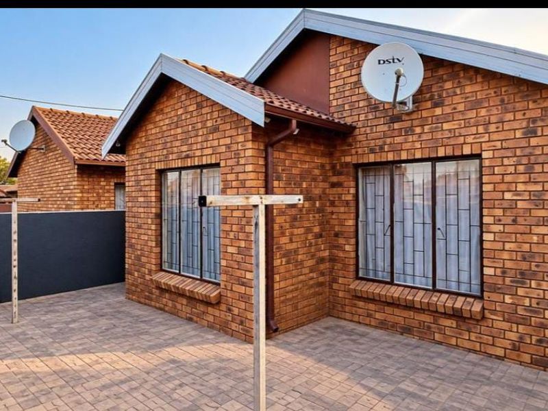 A well-maintained face brick exterior featuring a paved patio area, secure window bars, and tiled roofing.
