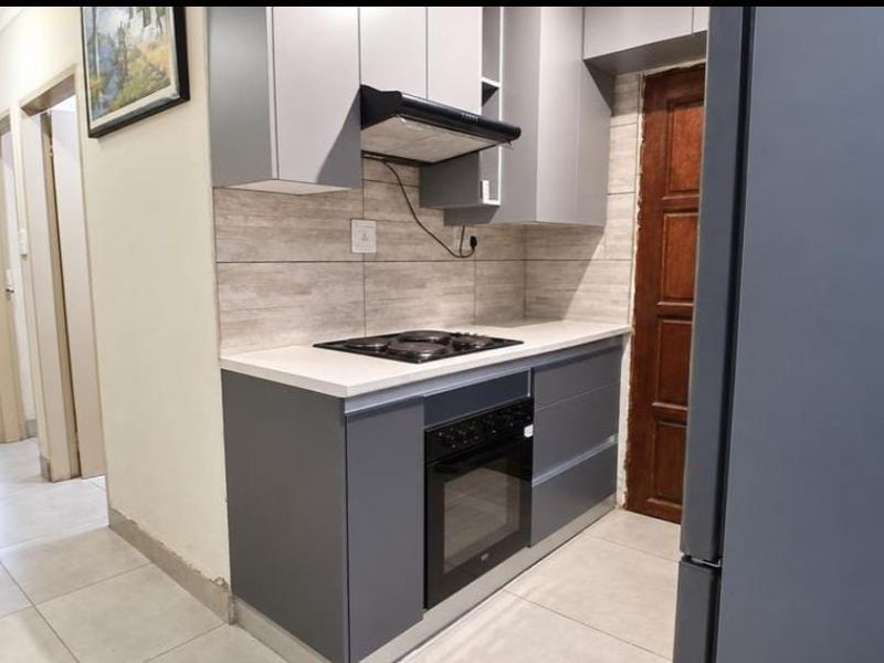Modern kitchen featuring grey cabinetry, stone countertops, built-in oven, electric hob, and extractor fan, with tiled flooring and a neutral backsplash.
