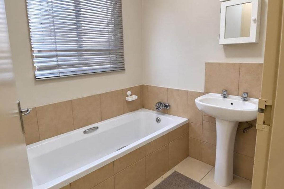A functional bathroom featuring a pedestal washbasin, a built-in bathtub with tiled surround, and a wall-mounted medicine cabinet.