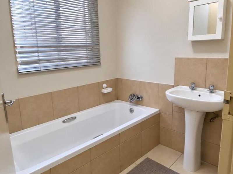 A functional bathroom featuring a pedestal washbasin, a built-in bathtub with tiled surround, and a wall-mounted medicine cabinet.