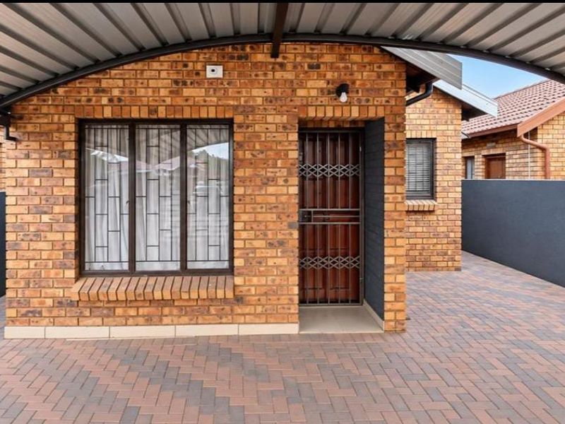 A well-maintained face brick exterior featuring a covered carport, paved driveway, and secure entrance with a metal security gate.
