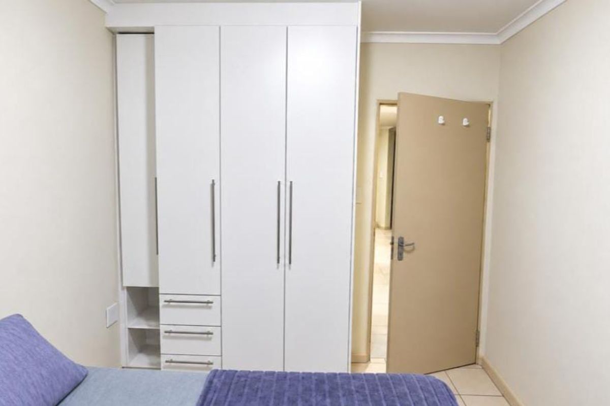 A bedroom featuring white built-in cupboards with integrated drawers and shelving, complemented by neutral wall finishes and tiled flooring.
