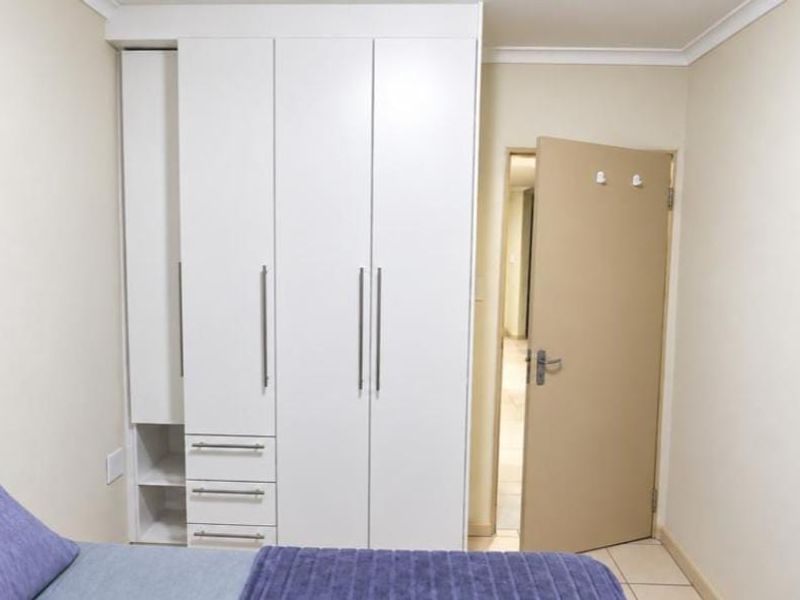 A bedroom featuring white built-in cupboards with integrated drawers and shelving, complemented by neutral wall finishes and tiled flooring.