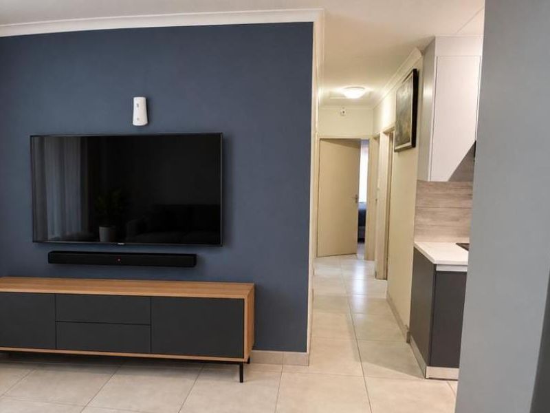 Modern open-plan living area featuring a dark accent wall, tiled flooring, and a sleek kitchen with contemporary cabinetry and stone countertops.