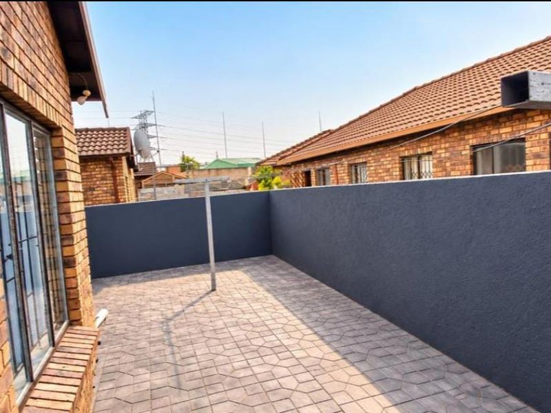 A private paved patio area featuring face brick walls, a modern dark boundary wall, and access via a sliding door.