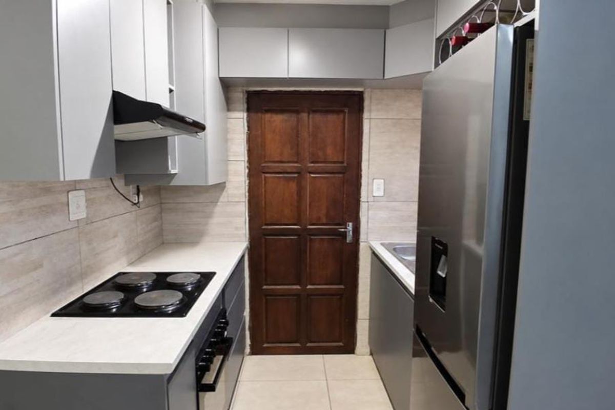 A modern galley-style kitchen featuring grey cabinetry, light countertops, a built-in electric hob, extractor fan, and tiled finishes throughout.