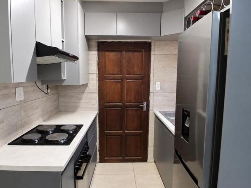 A modern galley-style kitchen featuring grey cabinetry, light countertops, a built-in electric hob, extractor fan, and tiled finishes throughout.