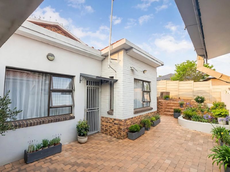 A well-maintained rear courtyard featuring brick paving, landscaped stepped garden beds, and a secure entrance with aluminum window frames.