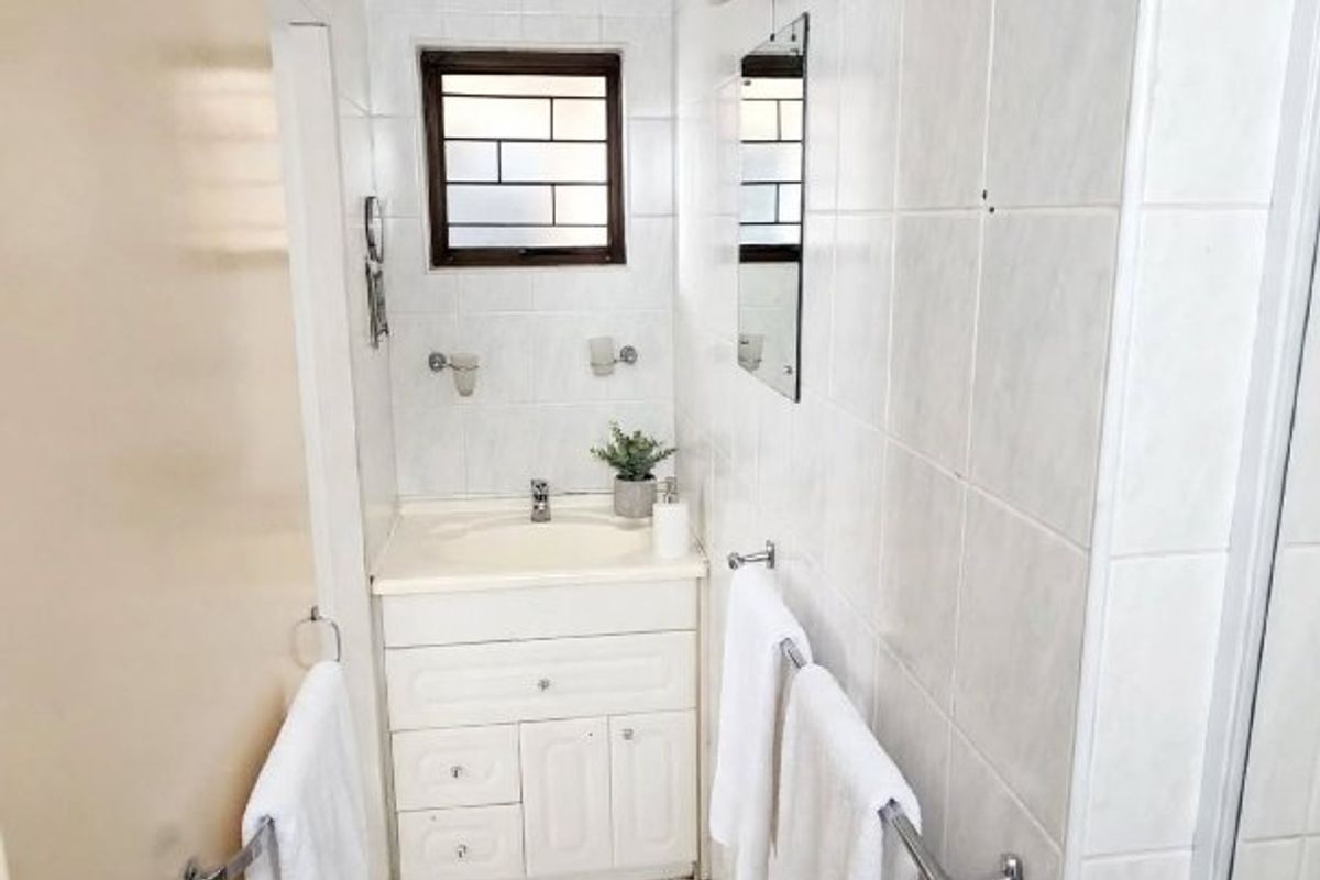 A compact bathroom featuring a vanity cabinet with a basin, tiled walls and flooring, and a window with security bars.