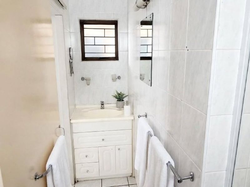 A compact bathroom featuring a vanity cabinet with a basin, tiled walls and flooring, and a window with security bars.