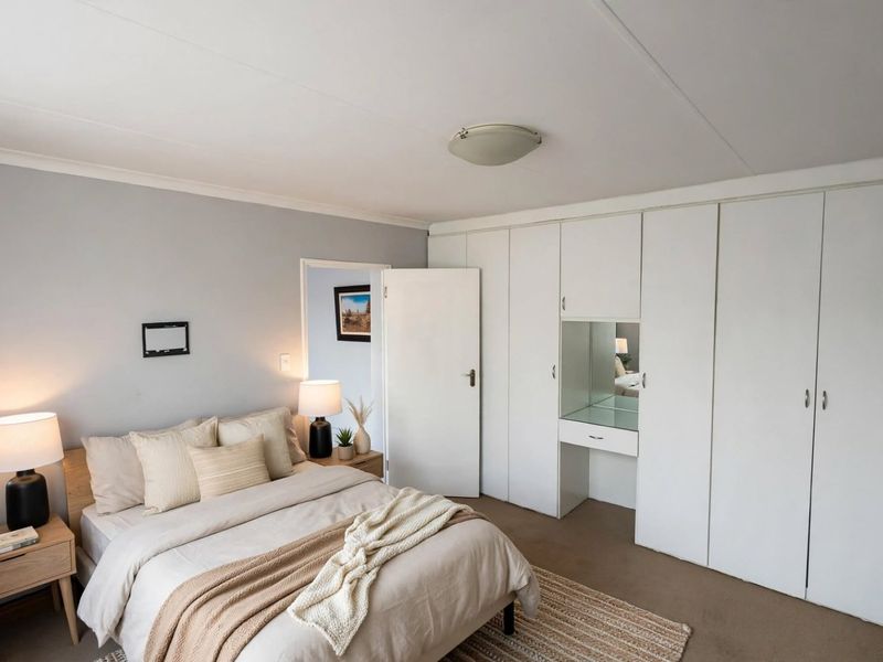 A well-lit bedroom featuring extensive built-in cupboards with an integrated vanity unit and neutral wall finishes.