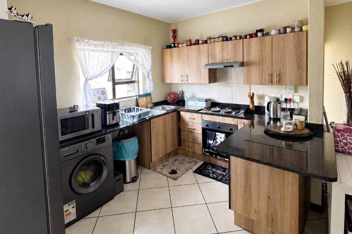 A functional kitchen featuring wood-finish cabinetry, granite countertops, built-in oven with hob, extractor fan, and tiled flooring.