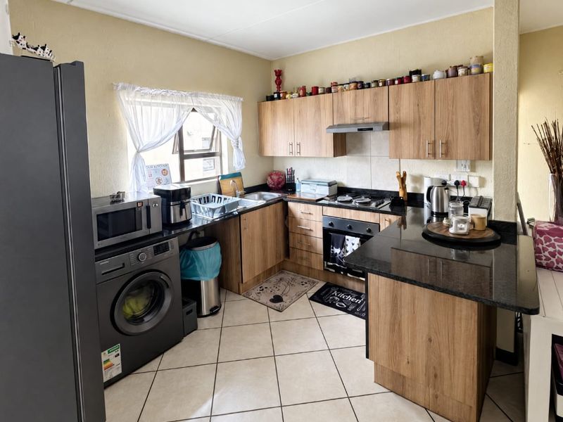 A functional kitchen featuring wood-finish cabinetry, granite countertops, built-in oven with hob, extractor fan, and tiled flooring.