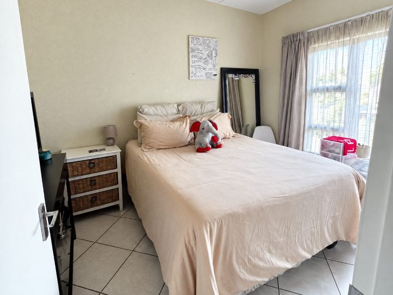 A functional bedroom featuring neutral tiled flooring, a large window with curtain treatments, and a standard ceiling light fixture.