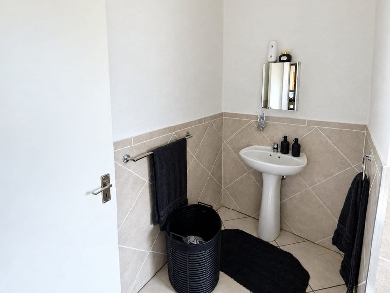 A compact bathroom featuring a pedestal basin, neutral wall and floor tiling, and a functional towel rail.