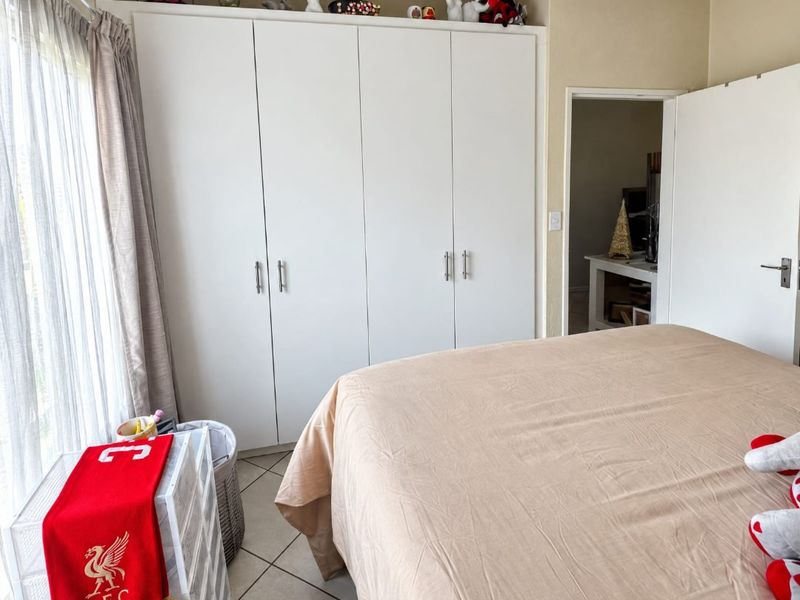 A bedroom featuring a large white built-in wardrobe with ample storage and neutral tiled flooring.