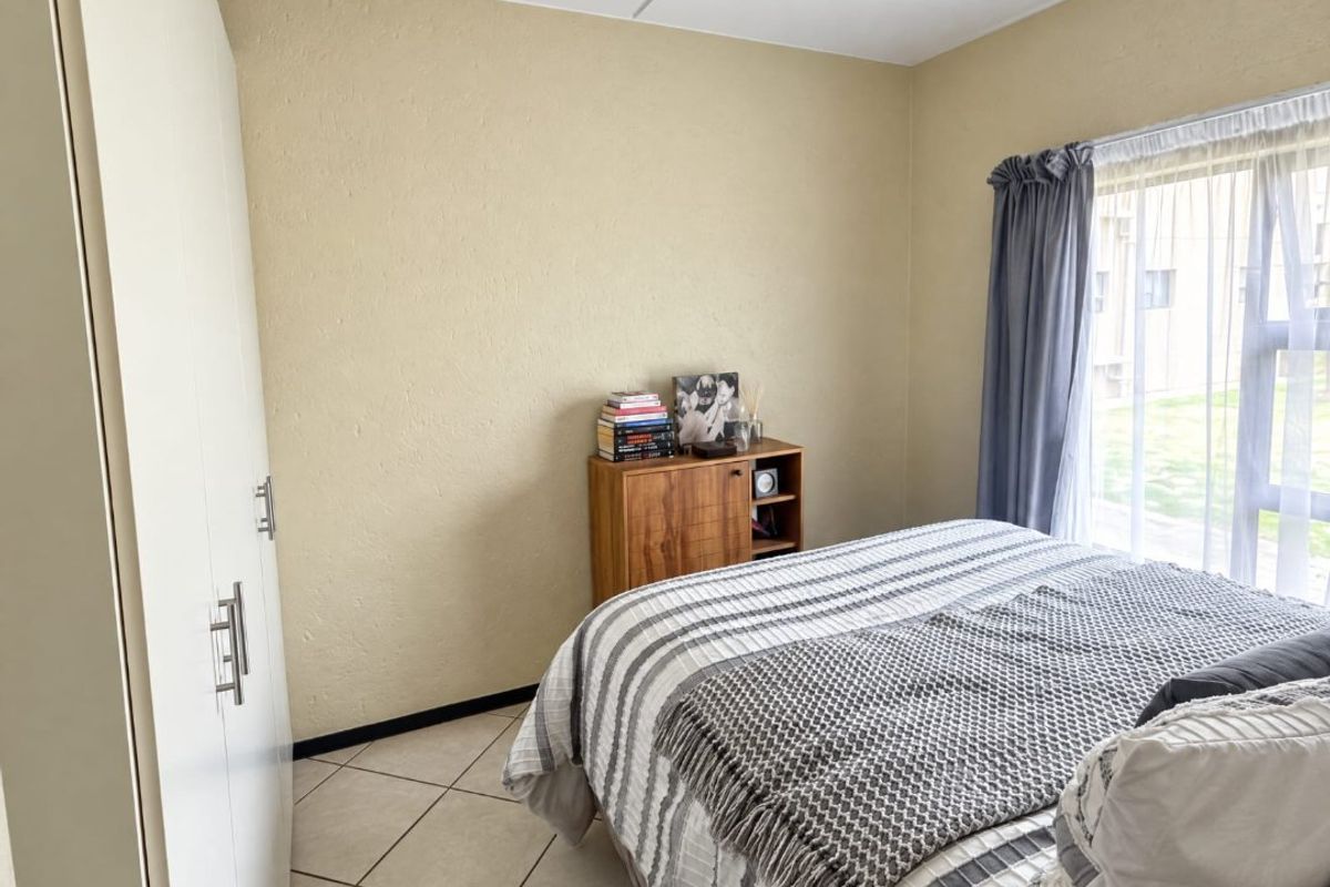 A functional bedroom featuring tiled flooring, a built-in wardrobe, and natural light from a large window.