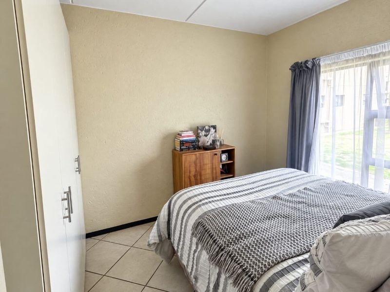 A functional bedroom featuring tiled flooring, a built-in wardrobe, and natural light from a large window.