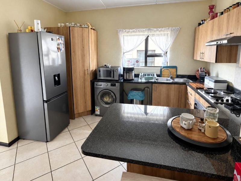 A functional kitchen featuring granite countertops, wood-finish cabinetry, a built-in hob with extractor fan, and tiled flooring.